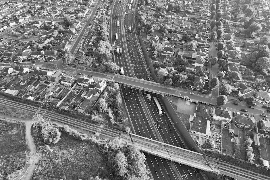 View of a city street taken from inside a building, showing a curved road with designated lanes for vehicles and tram tracks running along the middle. On the left side, there is a bus stop with a yell